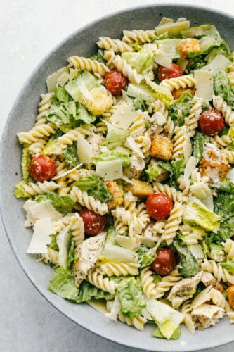 Chicken Caesar Pasta salad is fun twist on the classic! Fresh romaine tossed with chicken, cherry tomatoes, shredded parmesan cheese, croutons and a vegetable pasta adds a fun new texture! Caesar Salad with chicken and pasta in a bowl!