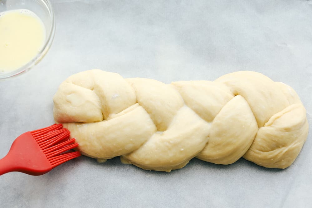 Challah Bread is a rich and fluffy loaf full of flavor. A Jewish traditional loaf, this incredible bread is going to be a favorite in your family baking! Putting an egg wash on raised dough.