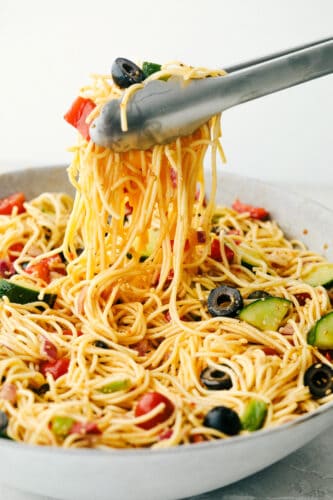 California Spaghetti Salad is a delicious pasta salad filled with fresh veggies and covered in a zesty Italian dressing. With all those flavors and colors making one beautiful and tasty side dish, there is no doubt this will be the hit of your next gathering! California spaghetti salad being lifted by the tongs.
