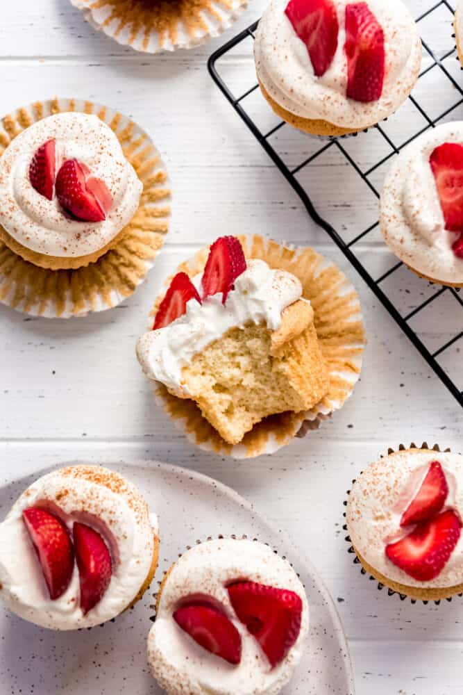 Light, fluffy Tres Leches Cupcakes are drenched in a three milk mixture, just like classic Tres Leches Cake, but in the handheld form! Topped with sweetened whipped cream, a light dusting of cinnamon, and fresh strawberries, these make a wonderful finish to any Mexican dinner! a cupcake with a bite taken out of it