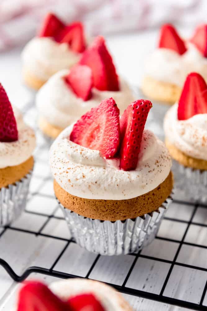 Light, fluffy Tres Leches Cupcakes are drenched in a three milk mixture, just like classic Tres Leches Cake, but in the handheld form! Topped with sweetened whipped cream, a light dusting of cinnamon, and fresh strawberries, these make a wonderful finish to any Mexican dinner! tres leches cupcakes on a wire rack