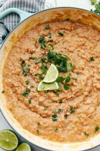 Homemade Refried Beans are simple and packed with so much flavor, you will never reach for a can again. These creamy refried beans are perfect for your next Tex-Mex night! A bowl of refried beans topped with cilantro and limes.