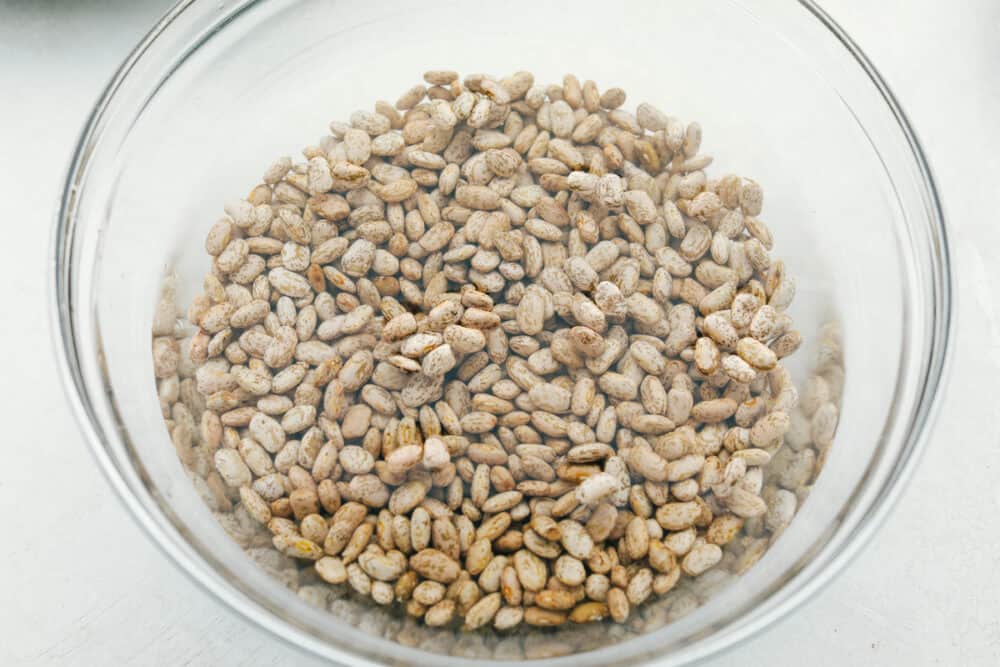 Homemade Refried Beans are simple and packed with so much flavor, you will never reach for a can again. These creamy refried beans are perfect for your next Tex-Mex night! Soaking dried beans in a glass bowl.