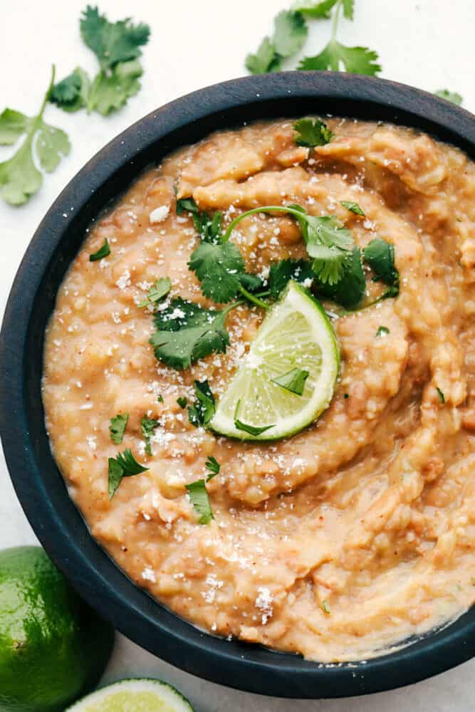 Homemade Refried Beans are simple and packed with so much flavor, you will never reach for a can again. These creamy refried beans are perfect for your next Tex-Mex night! A bowl of refried beans in a black bowl.