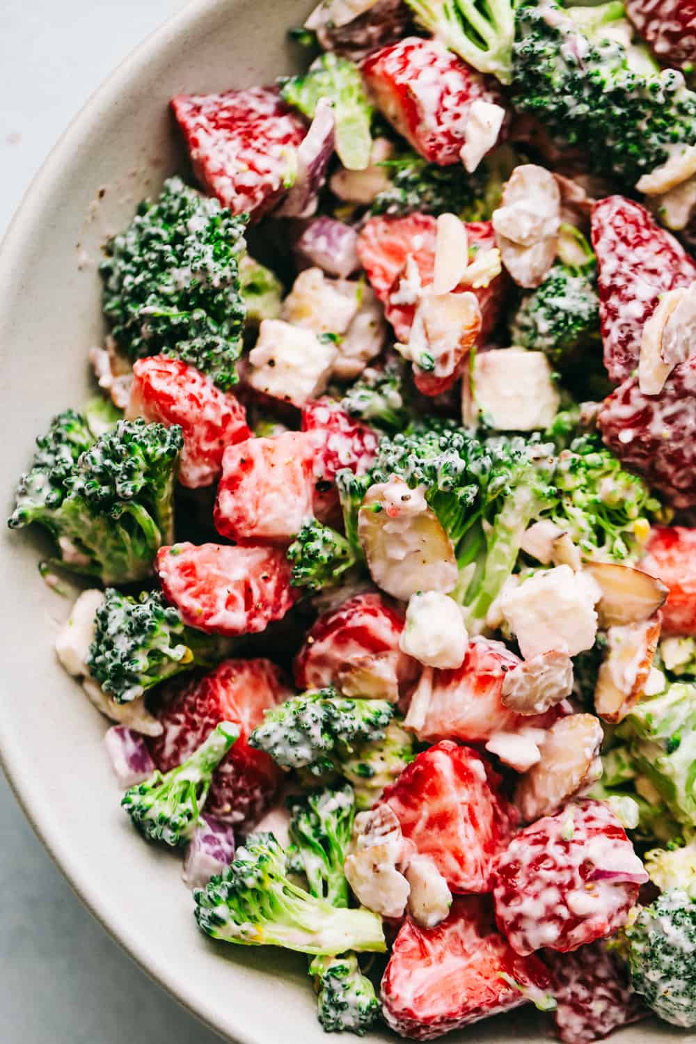 Creamy Broccoli Salad is a delicious broccoli salad with fresh strawberries, almonds, and feta cheese. Strawberries and broccoli combination create a sweet and savory salad with the creamy dressing on top makes it the best! Broccoli Strawberry salad in a white bowl mixed together.