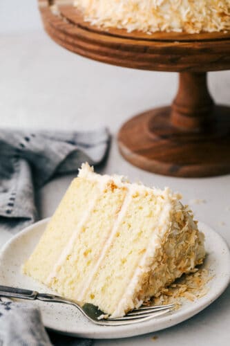 Coconut Cream Cake with Coconut Cream Cheese Frosting is super moist and delicious with the best coconut cream cheese frosting! This cake will be devoured and loved by all! A slice of coconut cake with frosting and toasted coconut on a plate.