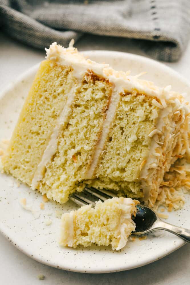 Coconut Cream Cake with Coconut Cream Cheese Frosting is super moist and delicious with the best coconut cream cheese frosting! This cake will be devoured and loved by all! A bite taken by a fork from a slice of cake.