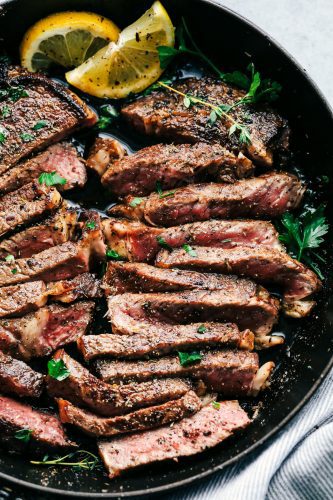 World's Best Steak Marinade adds so much flavor to your juicy steak. It helps to tenderize and infuse the steak with flavor and creates the best steak ever! Cut steak with steak marinade in a skillet with two slices of lemon.
