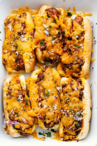 Baked Chili Cheese Dogs are like no other hot dog you have ever had! These are fast, easy and insanely delicious. A pan of baked chili dogs covered in cheese and red onions.