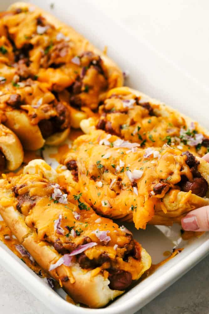 Baked Chili Cheese Dogs are like no other hot dog you have ever had! These are fast, easy and insanely delicious. Grabbing a chili cheese dog out of the pan to eat!