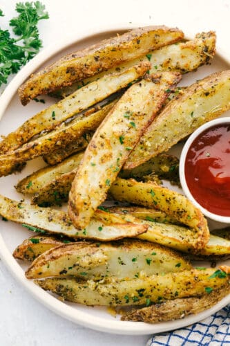 Air Fryer Potato Wedges are crispy and seasoned on the outside and perfectly tender on the inside! These are so insanely delicious you are going to love them! Air Fryer potato wedges on a plate with ketchup.