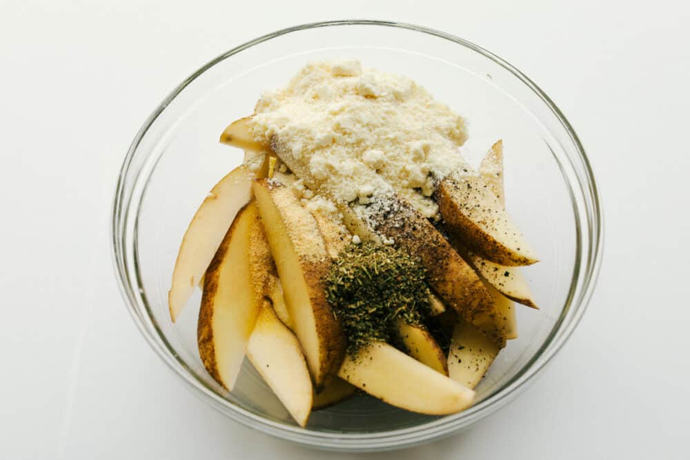 Air Fryer Potato Wedges are crispy and seasoned on the outside and perfectly tender on the inside! These are so insanely delicious you are going to love them! Potato wedges in a bowl with seasonings.