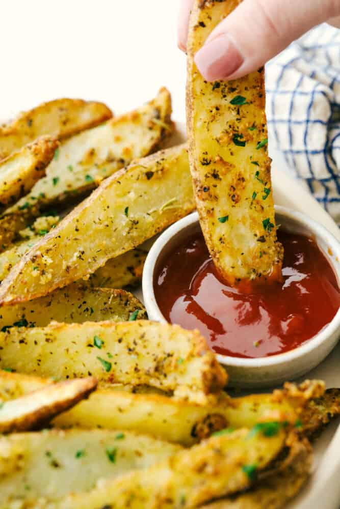 Air Fryer Potato Wedges are crispy and seasoned on the outside and perfectly tender on the inside! These are so insanely delicious you are going to love them! Dipping a potato wedge in some ketchup.