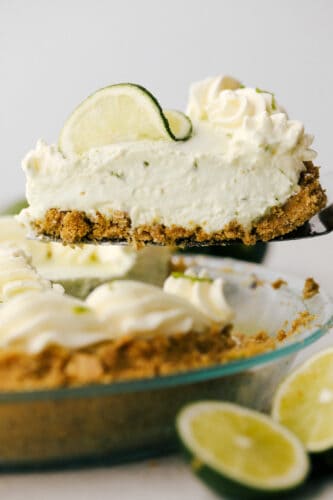 No Bake Key Lime PIe is a slice of tropical heaven. This has a sweet crunchy crust filled with a refreshing, creamy and zippy lime filling perfect for the summer heat! A slice of key lime pie being lifted from the tin.