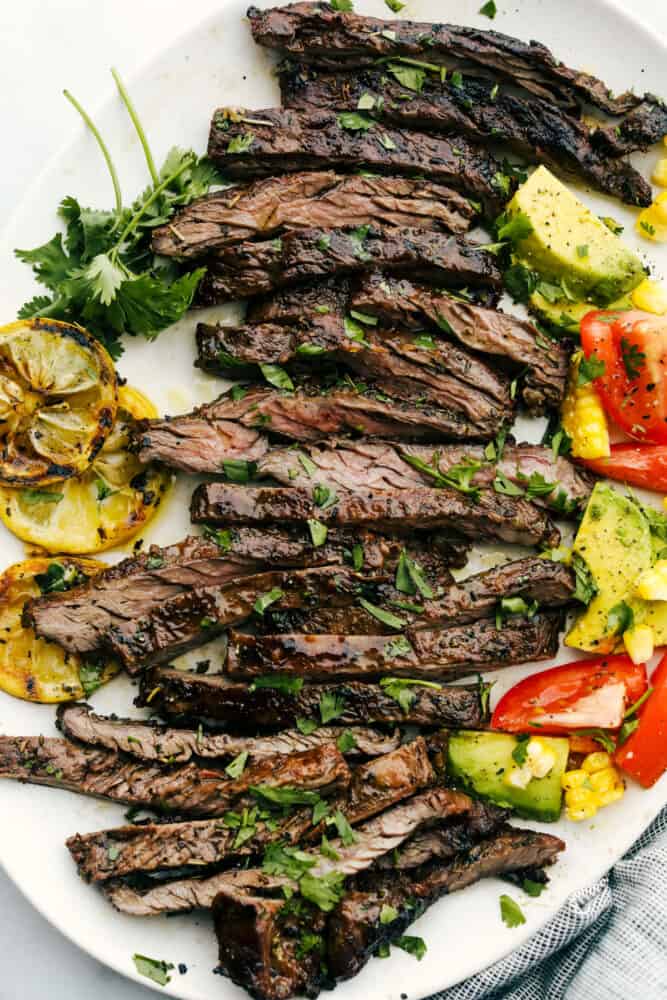 Grilled Skirt Steak is juicy, full of bold flavor, and absolutely delicious. Grilling skirt steak brings out the best of this long thin steak that you are going to love. Sliced grilled skirt steak on a plate with garnishes.