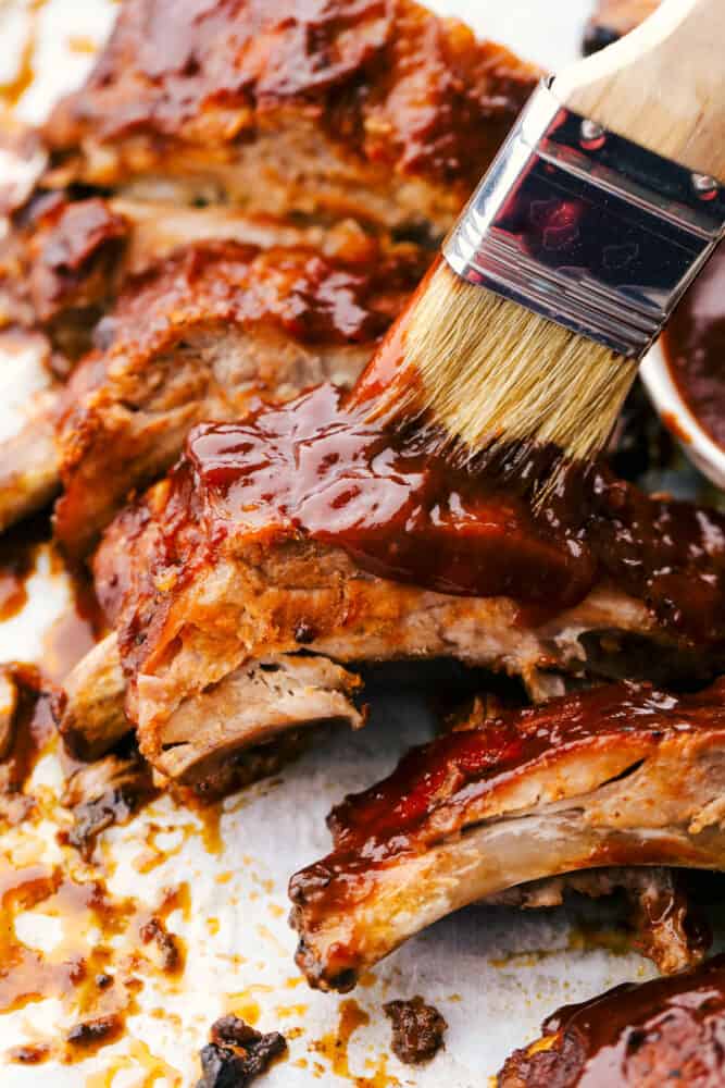 Slow Cooker ribs are going to melt in your mouth and fall off the bone! They are cooked low and slow so they are perfectly tender and then covered in a sauce that's absolutely to die for! Brushing on extra sauce on the slow cooker ribs.