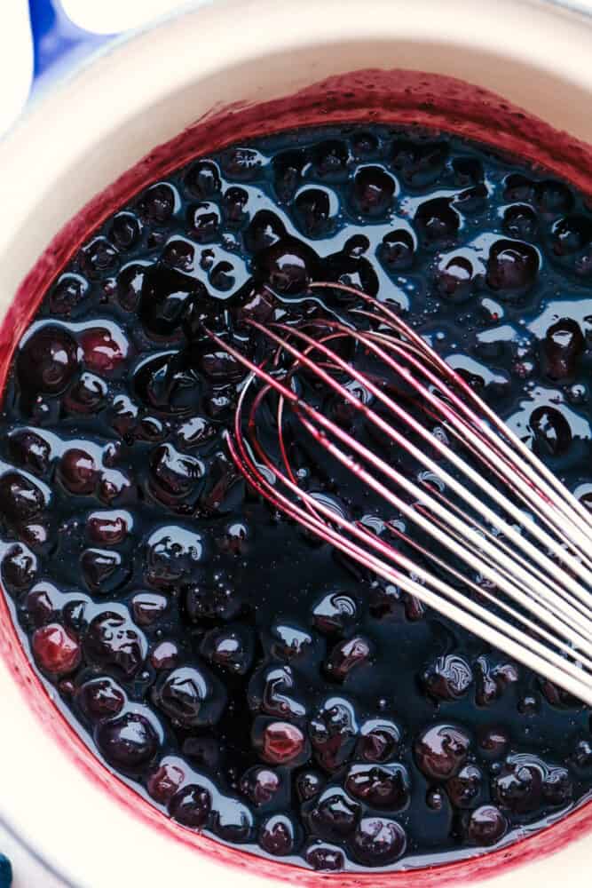 Homemade Blueberry Syrup will be the best addition to your breakfast lineup. It is sweet, decadent, and you will want to put it on everything! Blueberries being whisked in a bowl