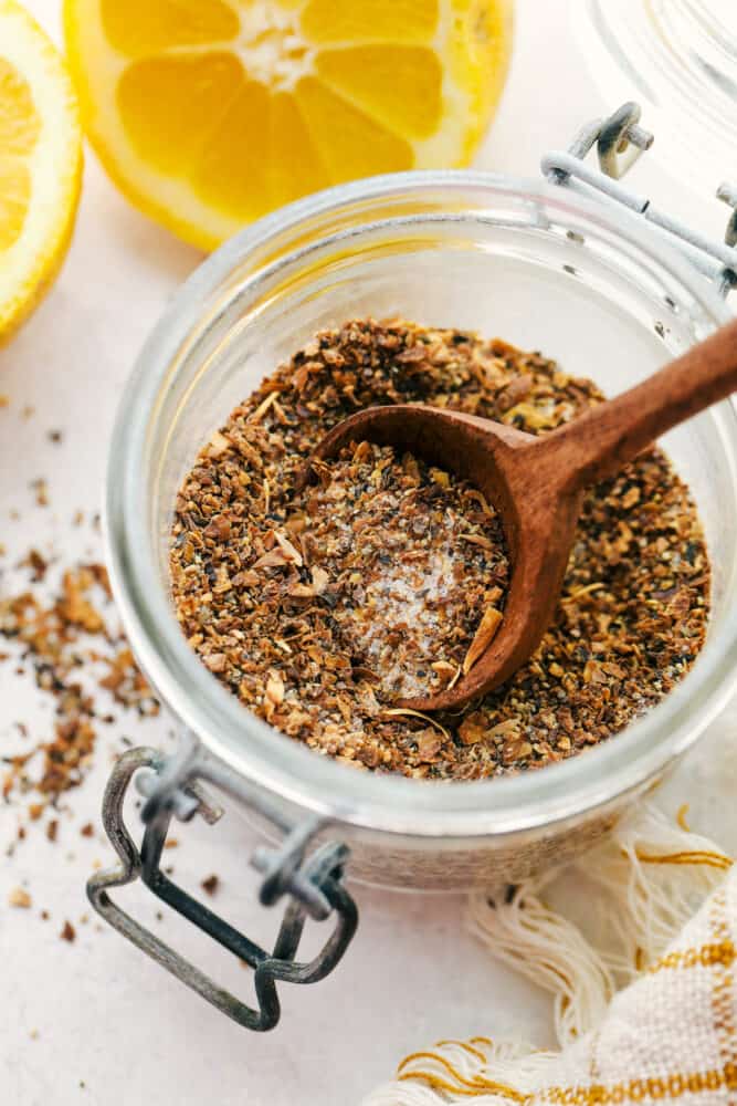 Lemon Pepper Seasoning is a little bit zingy and a little bit peppery, and a whole lot delightful! Making your own lemon pepper is super easy and absolutely delicious. Lemon pepper in a glass jar with a wooden spoon.
