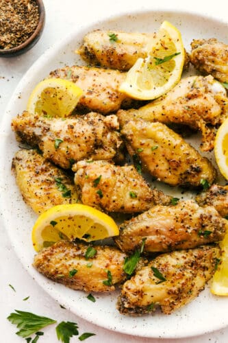 Lemon Pepper Chicken Wings are buttery, zesty, and will WOW at your next family get-together! They are super easy to make and pack delicious flavor in every juicy bite! Lemon Pepper Wings with lemon garnish on plate.