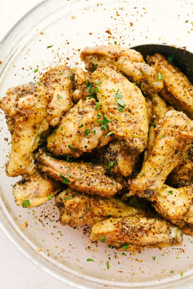 Lemon Pepper Chicken Wings are buttery, zesty, and will WOW at your next family get-together! They are super easy to make and pack delicious flavor in every juicy bite! Lemon Pepper Wings being tossed in bowl.