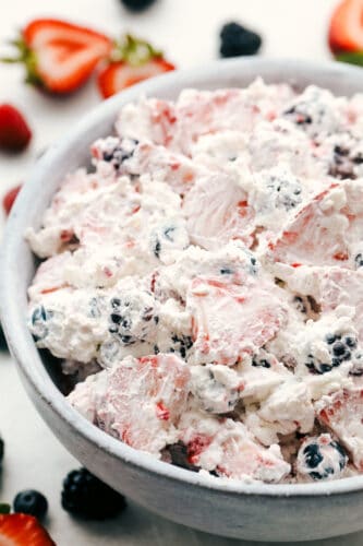 Berry Cheesecake Salad has only the freshest berries combined with a creamy cheesecake fluff. This is so amazing and will be the hit of any gathering! Berry cheesecake salad in a white bowl.