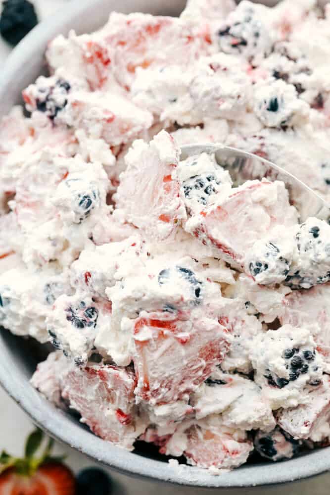 Berry Cheesecake Salad has only the freshest berries combined with a creamy cheesecake fluff. This is so amazing and will be the hit of any gathering! Scooping the berry cheesecake with a spoon.