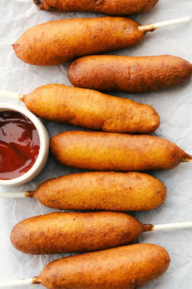 Homemade corn dogs are crispy golden on the outside and perfectly cooked on the inside. These are super easy to make at home and the whole family is going to love how they taste! Corn dogs lined up ready to eat with a side of ketchup.