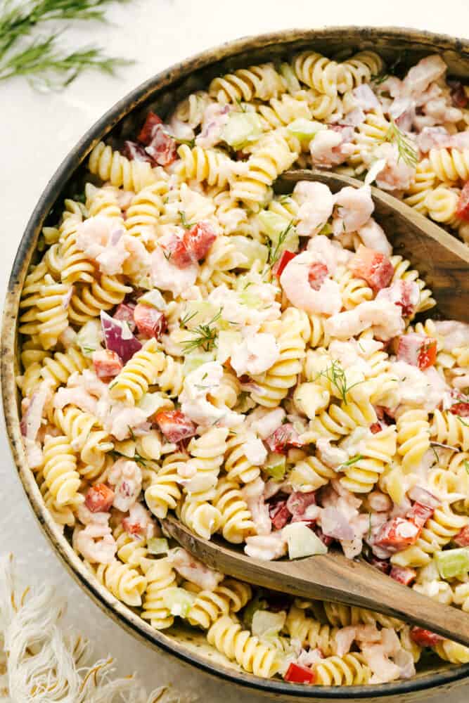 This Shrimp Pasta Salad is going to become your new go-to for summer picnics and potlucks. With tender bits of shrimp, fresh veggies, and the fact that it is so easy to put together and take on the go, it is quickly becoming one of my favorite recipes of the season! Shrimp pasta salad being mixed in a bowl