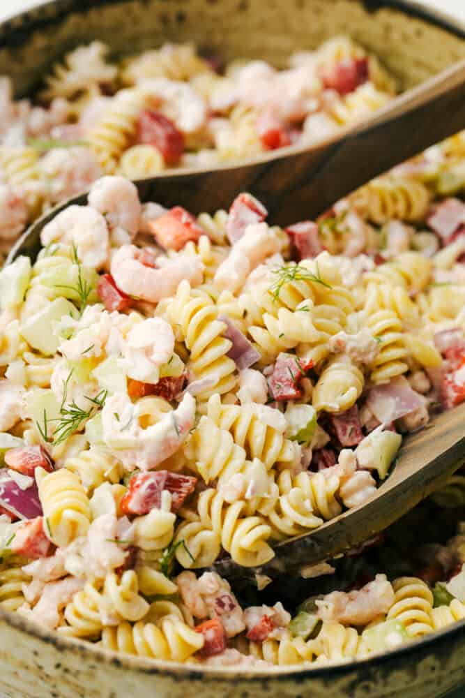 This Shrimp Pasta Salad is going to become your new go-to for summer picnics and potlucks. With tender bits of shrimp, fresh veggies, and the fact that it is so easy to put together and take on the go, it is quickly becoming one of my favorite recipes of the season! Up close photo with shrimp pasta salad and two wooden spoons in the salad.