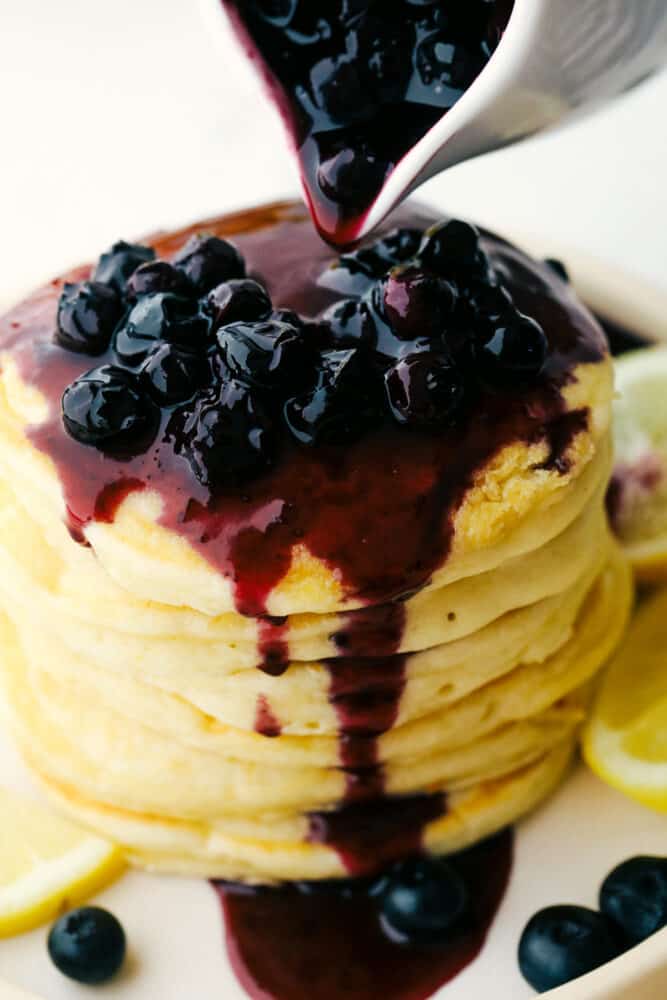 Lemon Ricotta Pancakes are fluffy, tender pancakes that are elevated to a whole new level. The ricotta adds protein and a lightness that is absolutely divine while the lemon gives it a bit of a tangy taste that you are going to love! Blueberry sauce drips down a stack of ricotta pancakes.