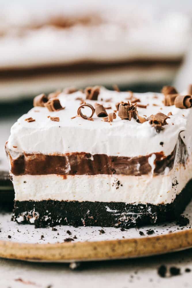 Oreo Lasagna is a no-bake slice of chocolate heaven! Layered with a cream cheese and pudding layer, sandwiched between whipped topping and luscious Oreo crust, it's too die for! A piece of Oreo Lasagna showing off the layers on a plate.
