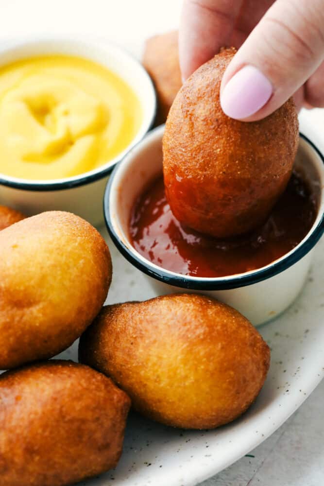 A crispy cornbread outer layer and snack-able size make these Mini Corn Dogs the perfect family treat! Recreate delicious county fair flavors in just a few simple steps! Mini corn dogs being dipped in ketchup.