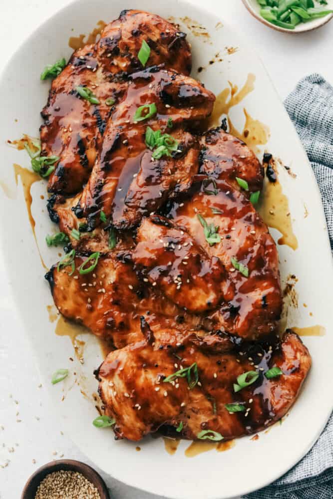 Grilled Teriyaki Chicken is the ultimate quick and easy, absolutely delicious dinner! Tender juicy chicken is soaked in the BEST Teriyaki Sauce then grilled to perfection Grilled teriyaki chicken breasts on a platter garnished with green onions and sesame seeds.