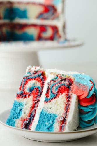 This Red, White and Blue Cake is going to steal the show for your 4th of July celebrations! Tender moist cake is swirled in the sweetest tie-dye pattern! A slice of the red white and blue cake showing the swirls.