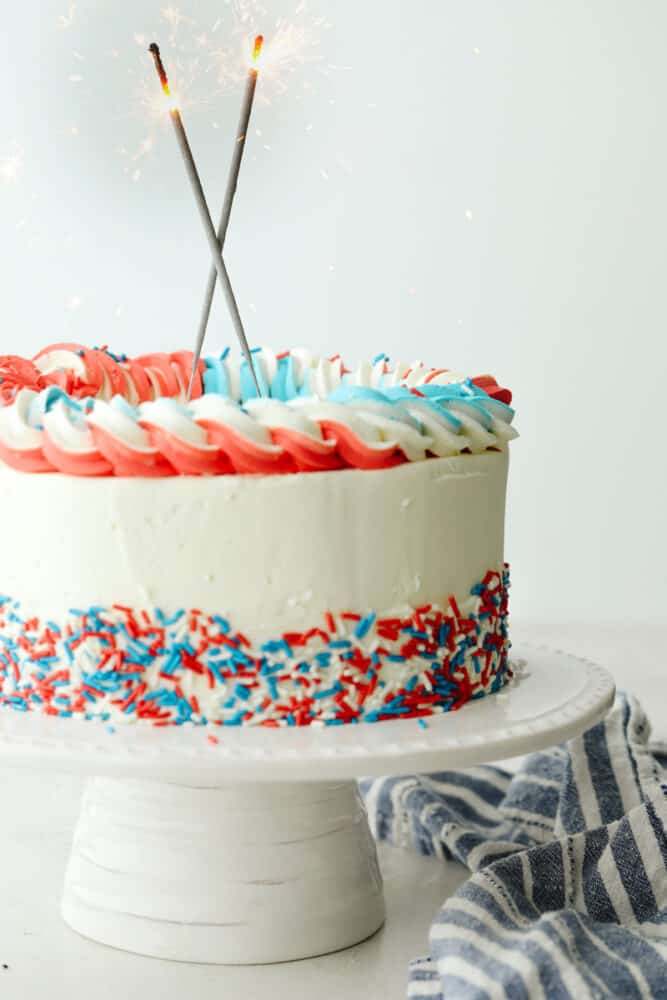 This Red, White and Blue Cake is going to steal the show for your 4th of July celebrations! Tender moist cake is swirled in the sweetest tie-dye pattern! Decorated cake with sparklers on top.