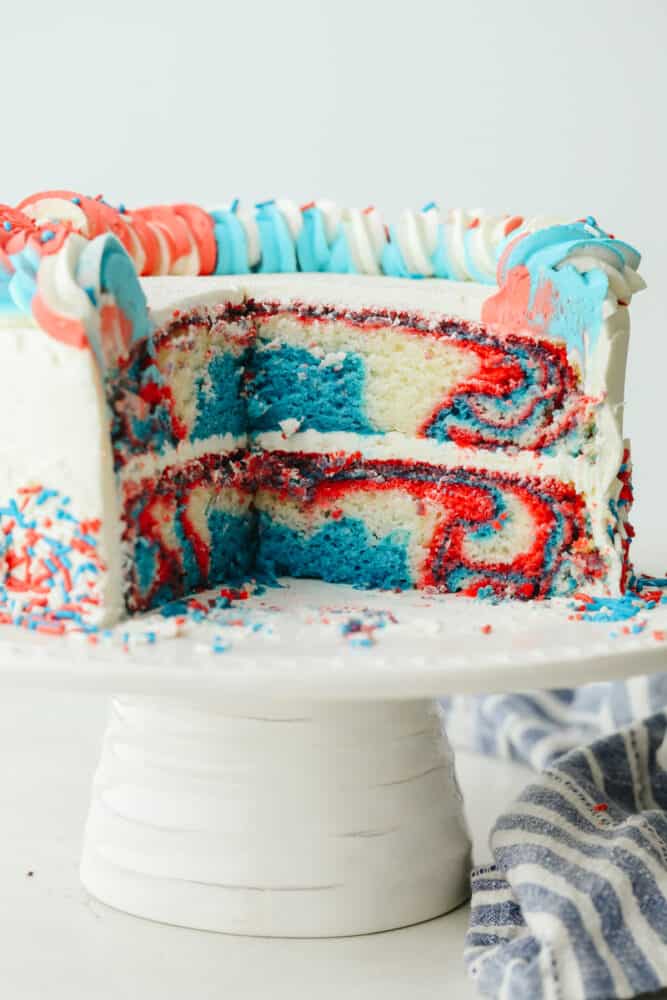 This Red, White and Blue Cake is going to steal the show for your 4th of July celebrations! Tender moist cake is swirled in the sweetest tie-dye pattern! The red, white, and blue cake sliced so you can see the inside.