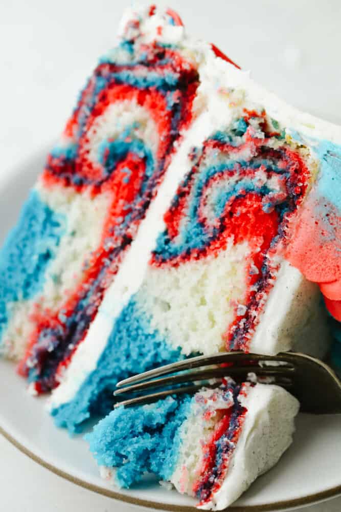 This Red, White and Blue Cake is going to steal the show for your 4th of July celebrations! Tender moist cake is swirled in the sweetest tie-dye pattern! Cutting into the cake with a fork.