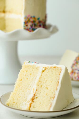 The Absolute Best White Cake is a recipe you will come back to time and time again for a delicious and beautiful result. Fluffy, moist, and soft, this really is a cake to impress! Slice of The Absolute Best White Cake.