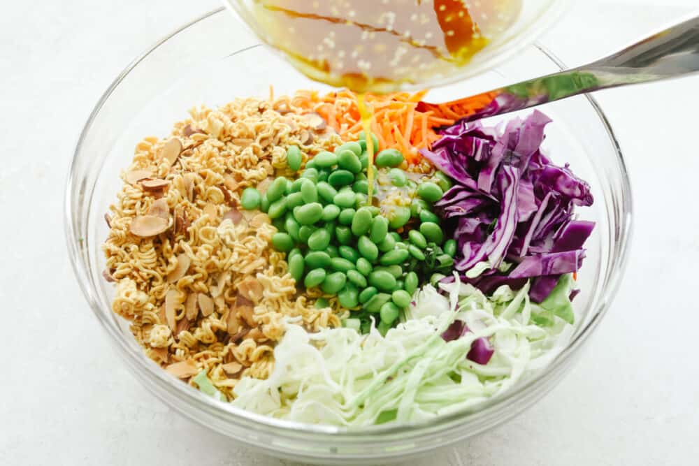Asian Ramen Salad is full of color, flavor, and crunch! All of the fun textures make it perfectly satisfying and insanely delicious! Pouring the dressing over the ingredients for Asian ramen salad.