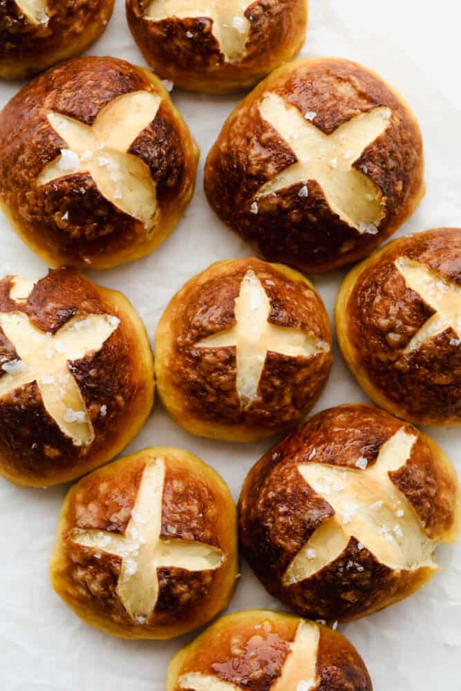 With a soft, tender inside and outside that has that cooked-to-perfection, pretzel texture we all love, these Pretzel Rolls are an instant favorite! Upgrade dinnertime with this irresistible side! Pretzel Rolls with coarse salt on parchment paper.
