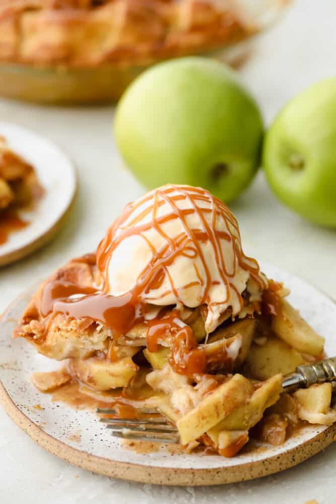 Caramel Apple Pie is the traditional American dessert, but totally elevated. Sour tart apples are smothered in caramel, it's insanely delicious. A slice of caramel apple pie with ice cream and caramel drizzled on top.