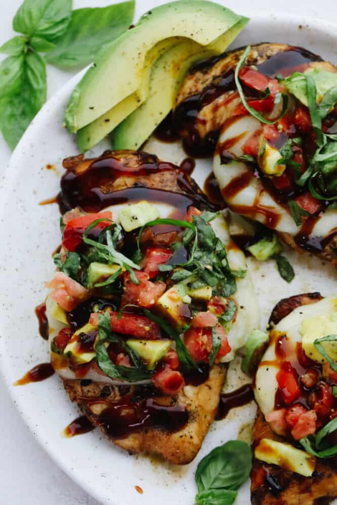 Grilled California Avocado Chicken is tender chicken marinated in an amazing honey garlic balsamic sauce and is grilled to perfection! Grilled California Avocado chicken on a white plate with basil and sliced avocado garnish.
