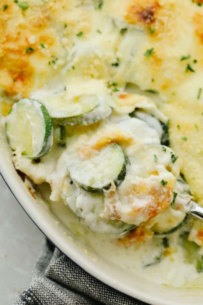 Three Cheese Zucchini Gratin has layers of creamy, cheesy sauce and is topped with a crunchy buttery topping. Ooey-gooey and cheesy, this low-carb take on comfort food will please any crowd! Taking a scoop of Parmesan Zucchini Gratin.