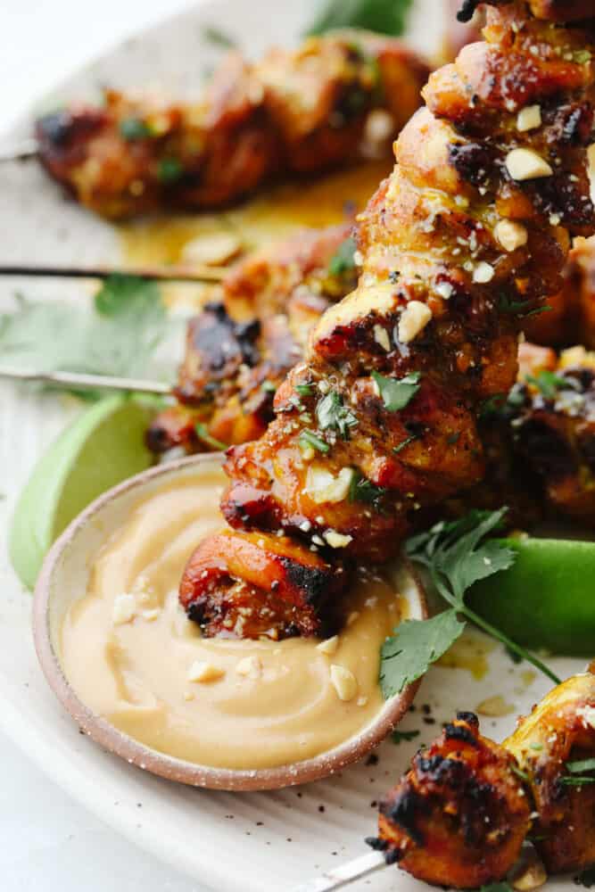 Chicken Satay is juicy, tangy, and absolutely divine. Marinated and then grilled to perfection serve these with a savory peanut sauce that is positively addicting. Dunking a chicken satay skewer in peanut sauce.