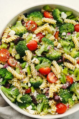Greek Broccoli Pasta Salad combines tender fusilli pasta with fresh vegetables and a tangy herb dressing. This is the perfect dish to serve with grilled meats, or pack for a picnic or barbecue! Greek broccoli pasta salad in a white bowl.