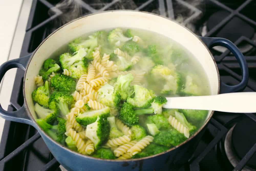 Greek Broccoli Pasta Salad combines tender fusilli pasta with fresh vegetables and a tangy herb dressing. This is the perfect dish to serve with grilled meats, or pack for a picnic or barbecue! Boiling broccoli and pasta in a pot.