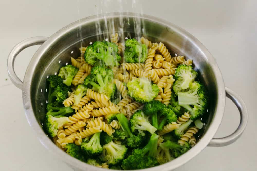 Greek Broccoli Pasta Salad combines tender fusilli pasta with fresh vegetables and a tangy herb dressing. This is the perfect dish to serve with grilled meats, or pack for a picnic or barbecue! Straining veggies and pasta and rinsing with cold water.
