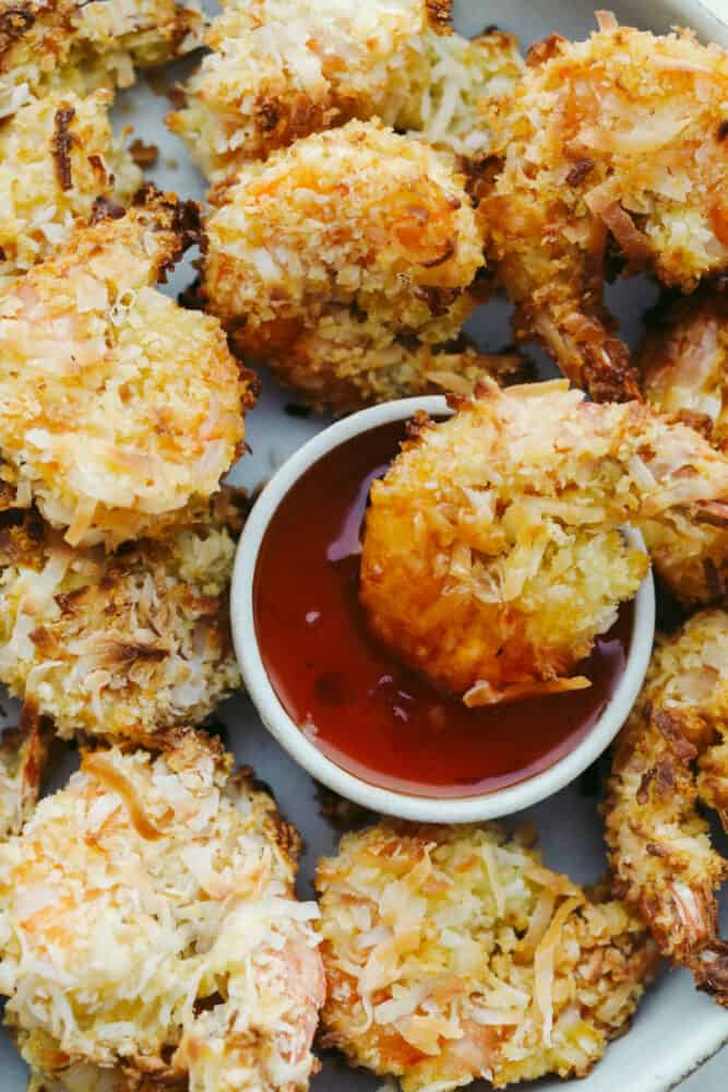 These super easy baked coconut shrimp will deliver in a flavor so delicious they will be sure to be a favorite among all of your guests! They are golden and crispy and baked to perfection. Shrimp and dipping sauce in serving dish.