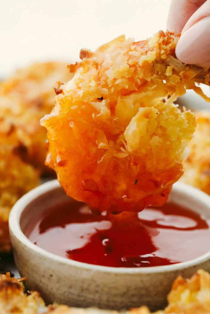 These super easy baked coconut shrimp will deliver in a flavor so delicious they will be sure to be a favorite among all of your guests! They are golden and crispy and baked to perfection. Baked Coconut Shrimp being dipped in sauce.