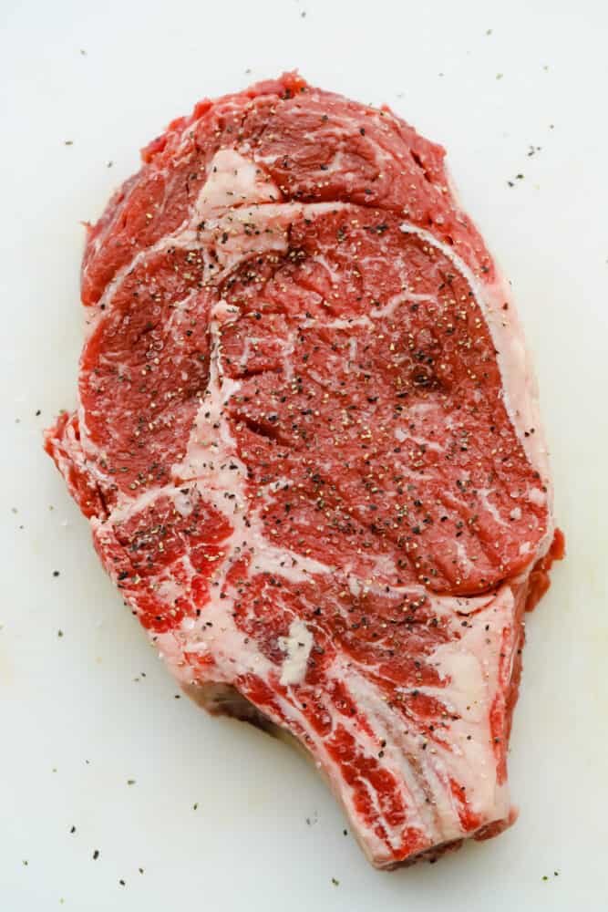 Achieving steakhouse-worthy flavors doesn’t have to be difficult! The ultimate ribeye steak is juicy, flavorful, and seared to perfection all in the comfort of your kitchen. A raw ribeye steak salted and peppered.